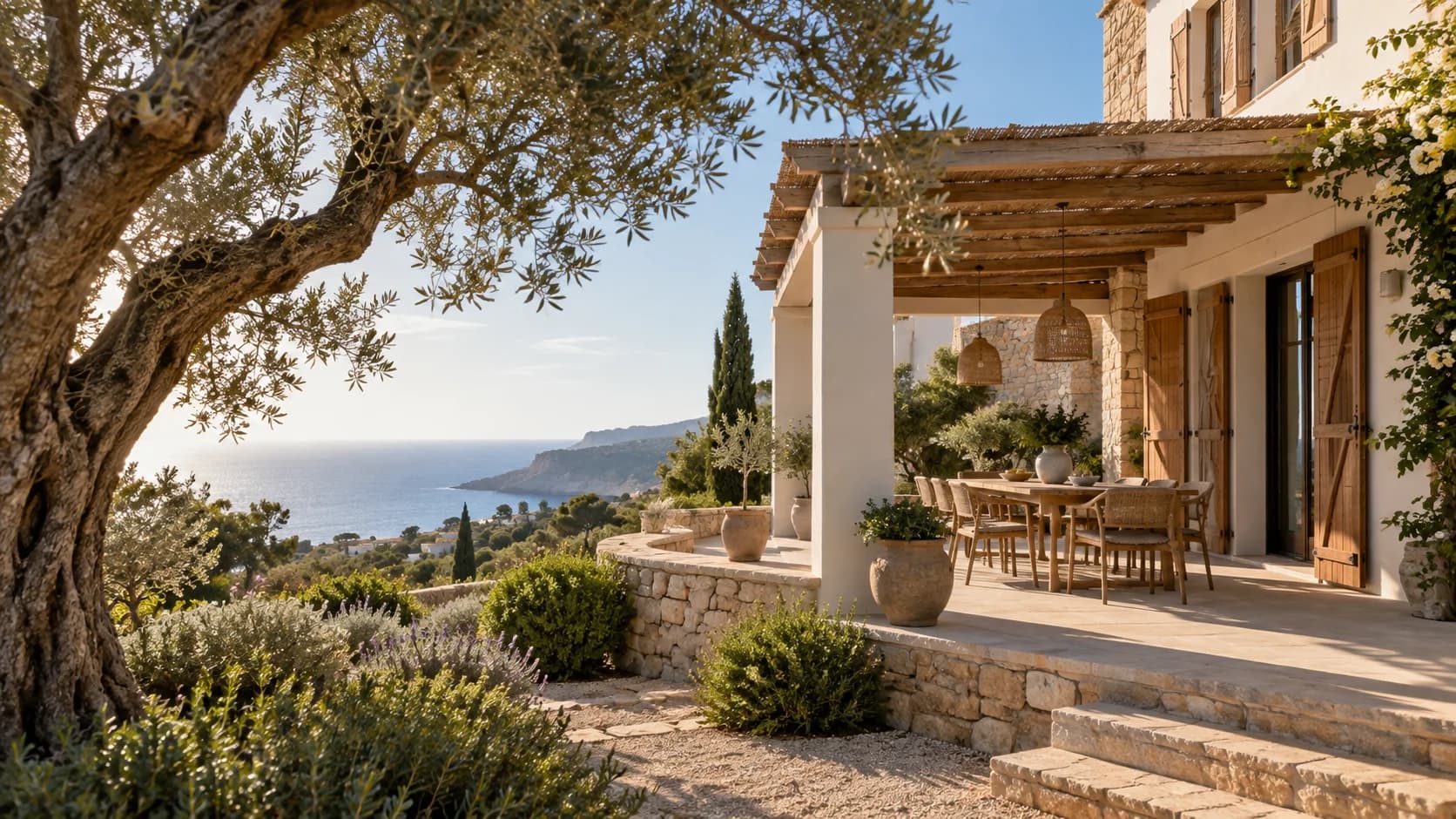 Vivienda mediterránea con una terraza a la sombra, un olivo y vistas al mar.